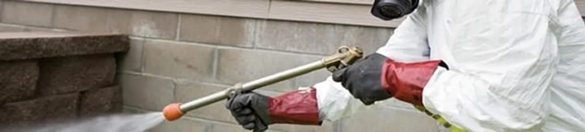 Pest control technician applying exterior insect treatment along a home foundation in Omaha, NE