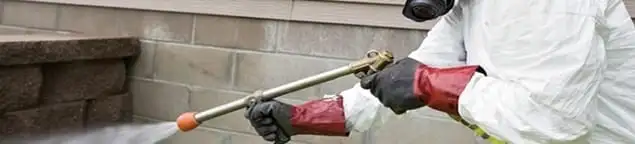 Pest control technician applying exterior insect treatment along a home foundation in Omaha, NE