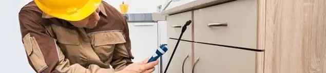 Roach exterminator applying treatment under kitchen cabinets in Omaha, NE