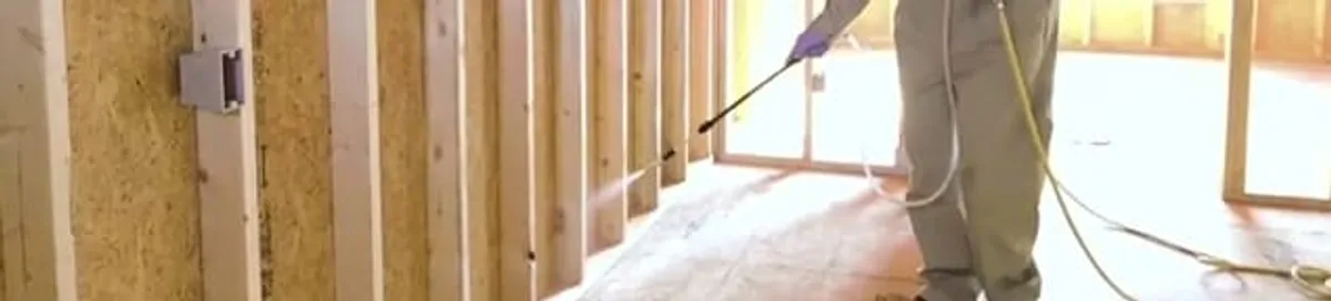 Termite treatment technician applying spray along framing and unfinished walls in Omaha, NE