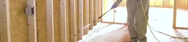 Termite treatment technician applying spray along framing and unfinished walls in Omaha, NE